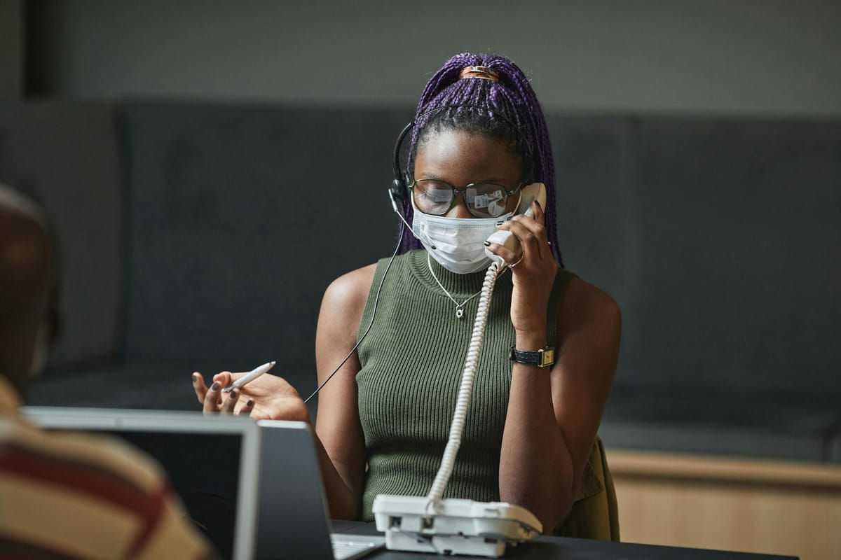 Woman with purple braided hair on a call in an office, wearing a mask for safety.